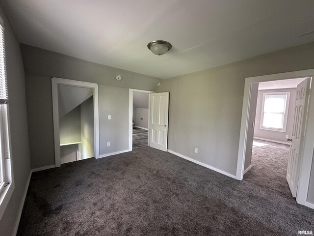 unfurnished bedroom with dark carpet, baseboards, and vaulted ceiling