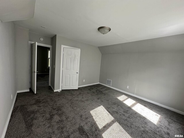 unfurnished bedroom featuring dark carpet, baseboards, and vaulted ceiling