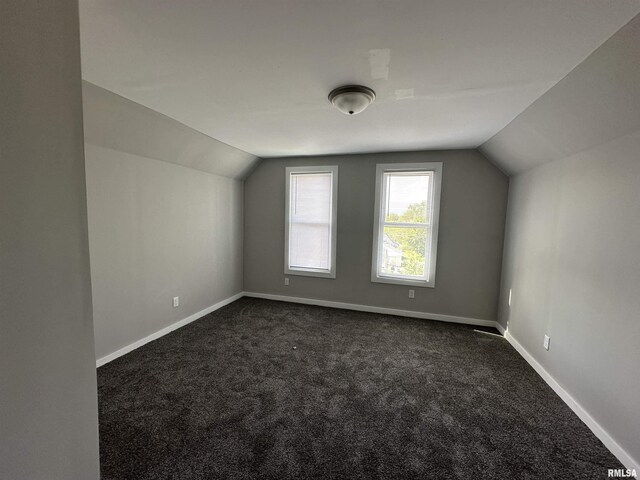 additional living space with vaulted ceiling, dark colored carpet, and baseboards