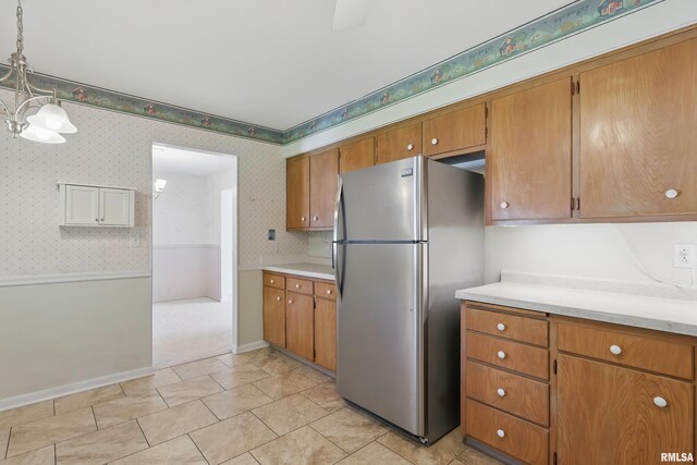 kitchen with freestanding refrigerator, wallpapered walls, brown cabinets, light countertops, and baseboards