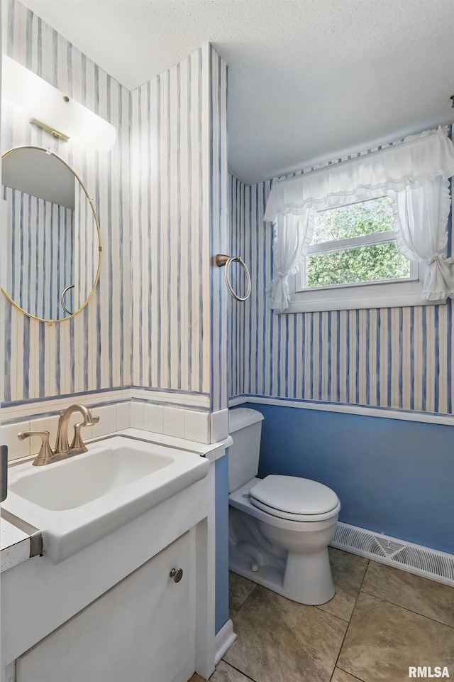 half bathroom featuring wallpapered walls, toilet, vanity, a textured ceiling, and tile patterned floors