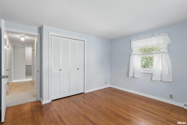unfurnished bedroom with wood finished floors, baseboards, and a closet