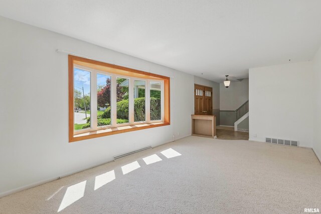 unfurnished living room featuring carpet flooring, baseboard heating, and stairway