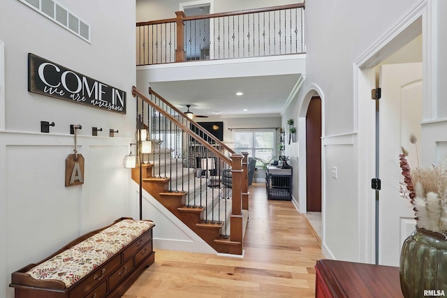 entrance foyer featuring light wood-type flooring, ceiling fan, stairs, a high ceiling, and arched walkways
