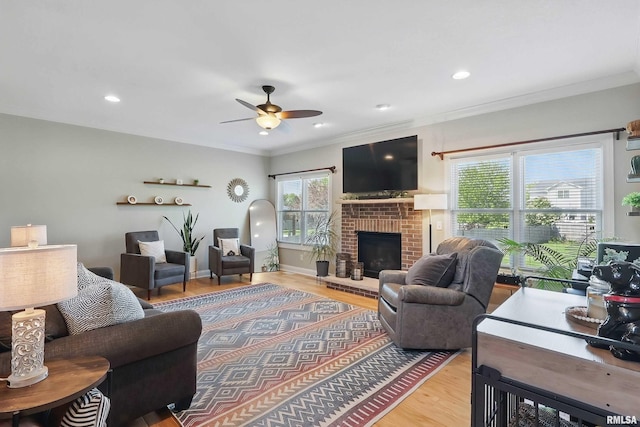 living area with wood finished floors, ceiling fan, crown molding, a brick fireplace, and recessed lighting