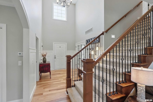 stairs with a high ceiling, wood finished floors, arched walkways, and a chandelier