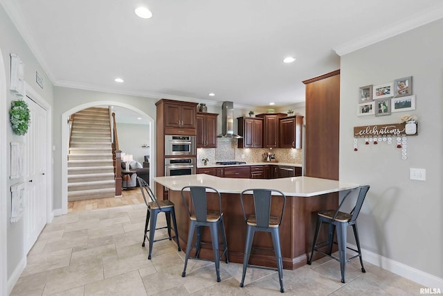 kitchen with wall chimney exhaust hood, arched walkways, a breakfast bar, light countertops, and crown molding