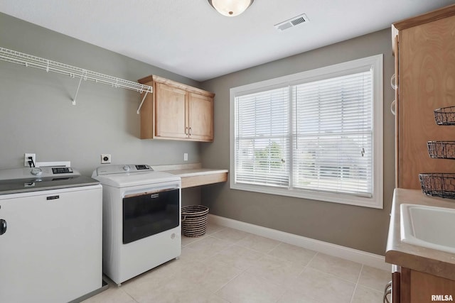 washroom featuring cabinet space, washing machine and clothes dryer, baseboards, and light tile patterned flooring