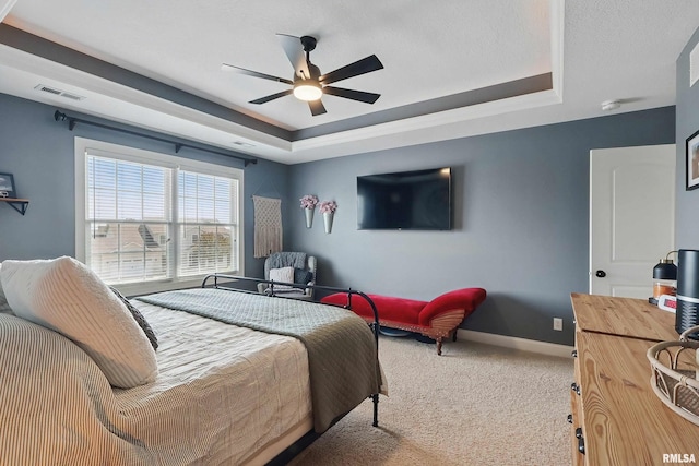 bedroom featuring a raised ceiling, carpet floors, baseboards, and a ceiling fan