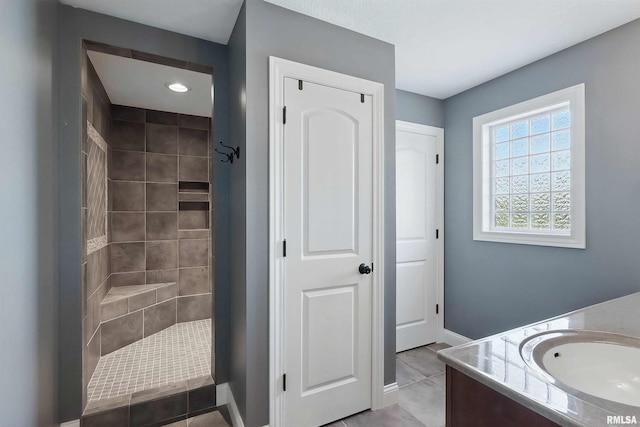 full bath featuring a tile shower, vanity, tile patterned floors, and baseboards
