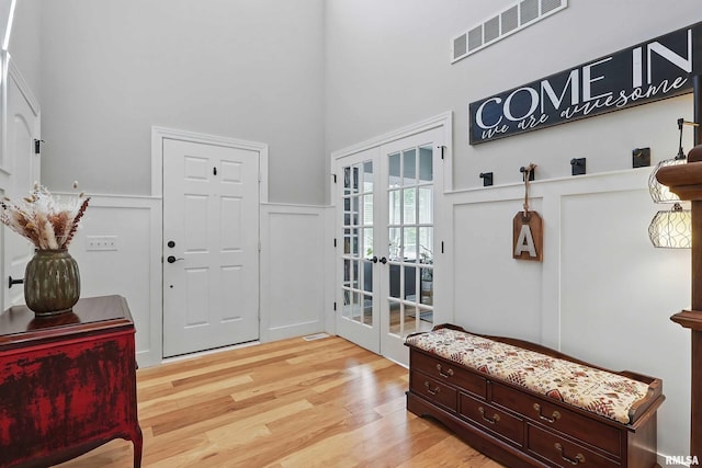 mudroom with french doors, wainscoting, light wood finished floors, a decorative wall, and a high ceiling