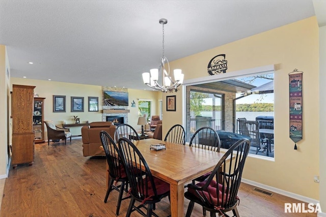 dining area with a chandelier, wood finished floors, baseboards, a warm lit fireplace, and recessed lighting