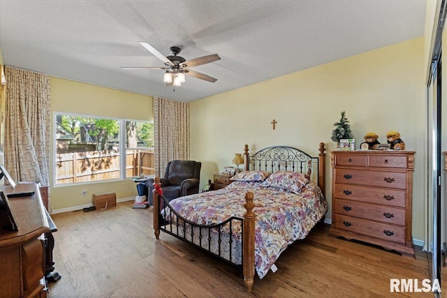 bedroom featuring wood finished floors, a textured ceiling, a ceiling fan, and baseboards