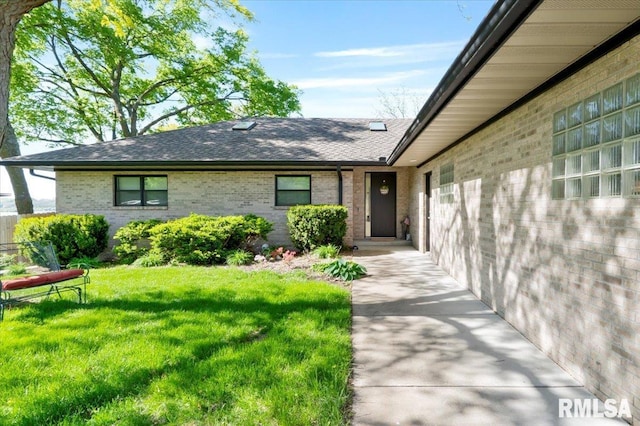 property entrance featuring roof with shingles, brick siding, and a lawn