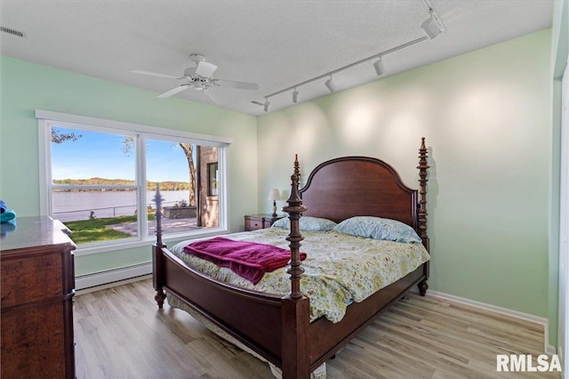 bedroom featuring a baseboard heating unit, track lighting, and wood finished floors