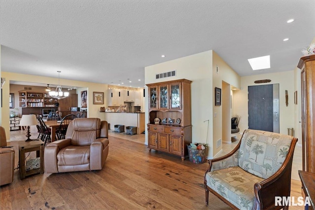 living room featuring a chandelier, wood finished floors, a textured ceiling, recessed lighting, and a skylight