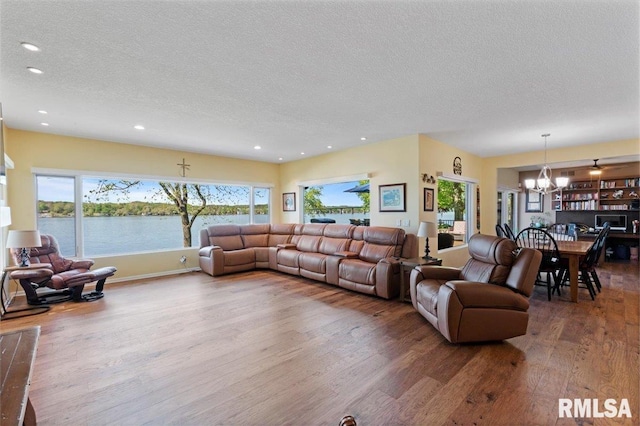 living room featuring a chandelier, wood finished floors, a textured ceiling, recessed lighting, and a water view