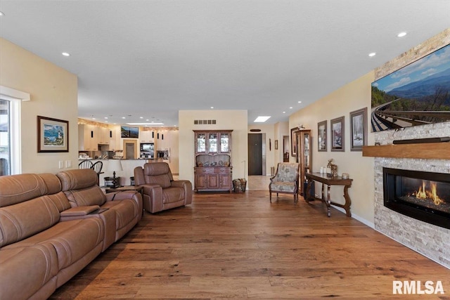 living room featuring wood finished floors, a stone fireplace, and recessed lighting