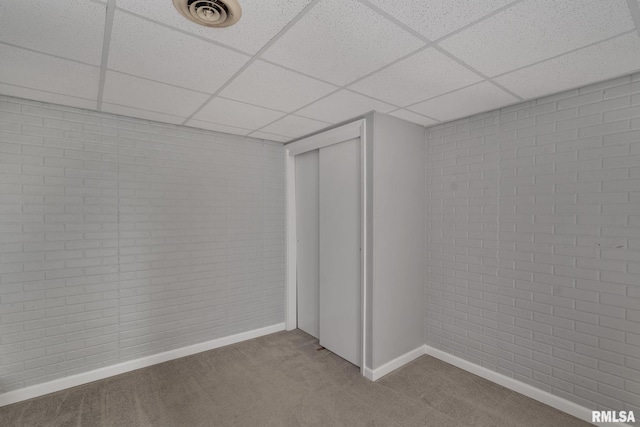 finished basement featuring a paneled ceiling, carpet flooring, baseboards, and brick wall