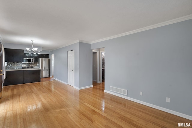 unfurnished living room with a chandelier, ornamental molding, light wood-style floors, and baseboards