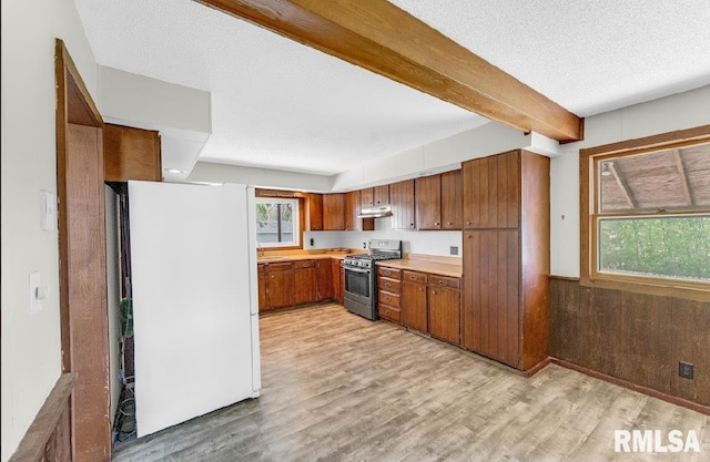 kitchen featuring stainless steel gas stove, freestanding refrigerator, brown cabinetry, light wood finished floors, and light countertops