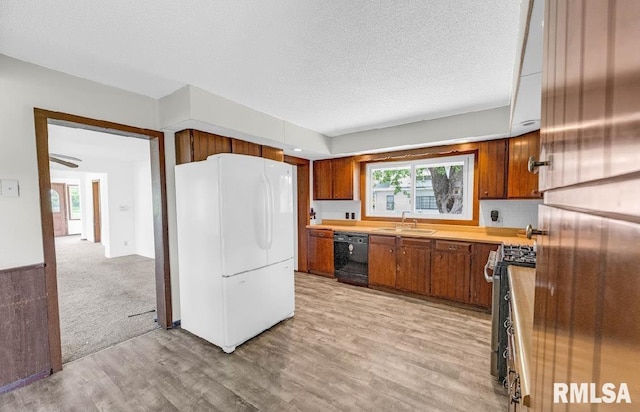 kitchen with freestanding refrigerator, black dishwasher, stainless steel gas stove, a sink, and light countertops