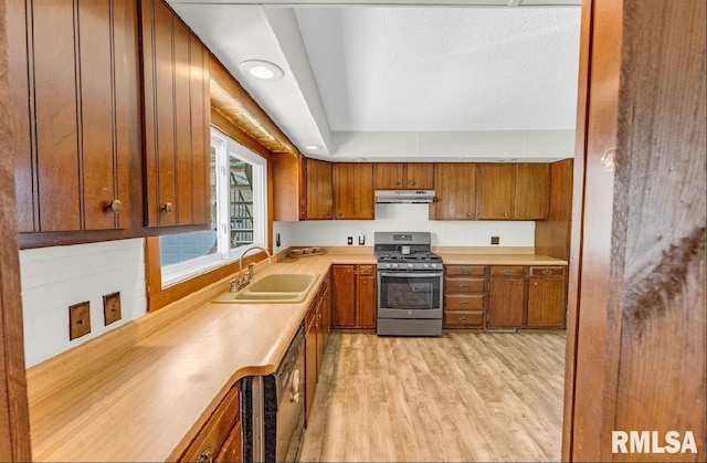 kitchen with stainless steel gas stove, a sink, under cabinet range hood, brown cabinets, and light wood-style floors