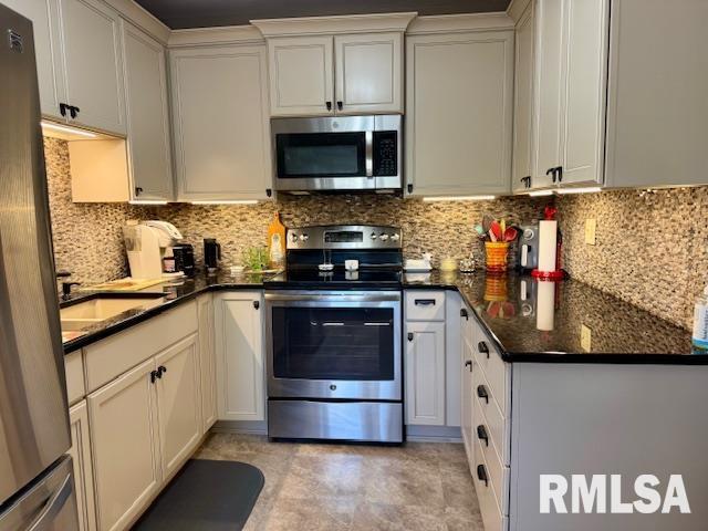 kitchen with appliances with stainless steel finishes, backsplash, a sink, dark stone countertops, and white cabinets