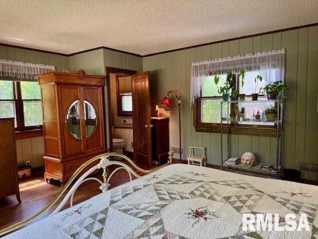 bedroom featuring a textured ceiling, wood finished floors, crown molding, and a decorative wall