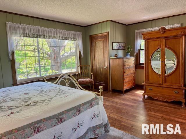 bedroom with a textured ceiling, wood finished floors, and crown molding