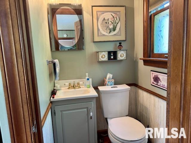 half bathroom featuring toilet, vanity, and wainscoting