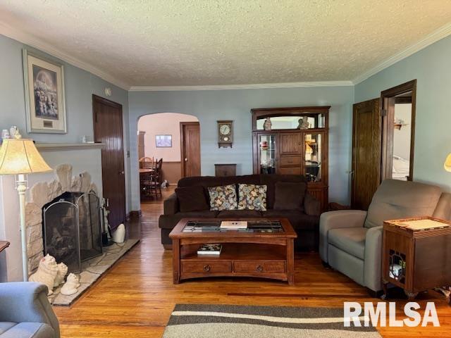living room with arched walkways, wood finished floors, a textured ceiling, a fireplace with raised hearth, and crown molding