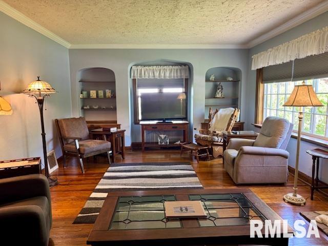 living area with built in features, a textured ceiling, wood finished floors, ornamental molding, and baseboards