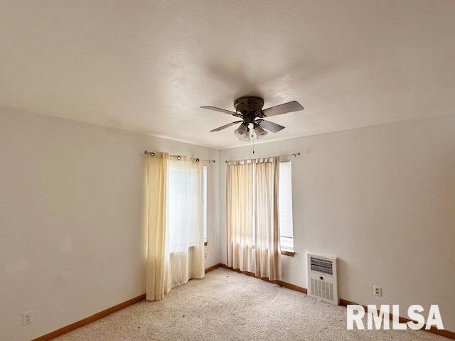 spare room featuring a ceiling fan, light carpet, baseboards, and heating unit