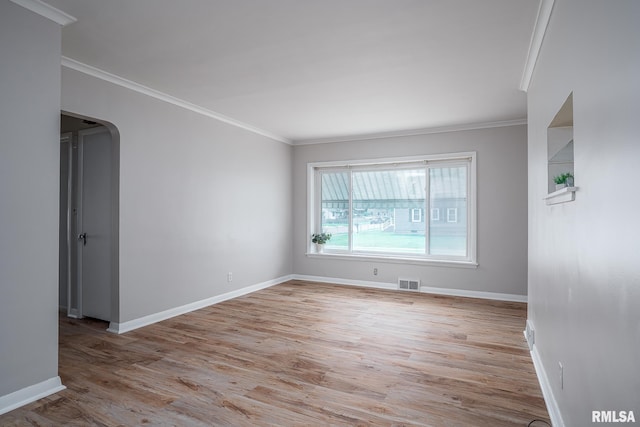 spare room featuring wood finished floors, crown molding, arched walkways, and baseboards