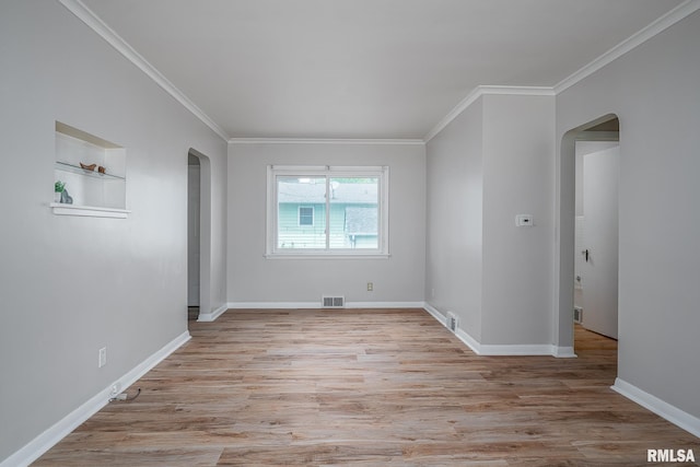 spare room featuring arched walkways, ornamental molding, light wood-type flooring, baseboards, and built in features