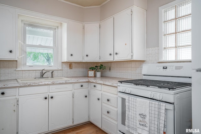 kitchen featuring white gas range, a sink, white cabinets, and ornamental molding