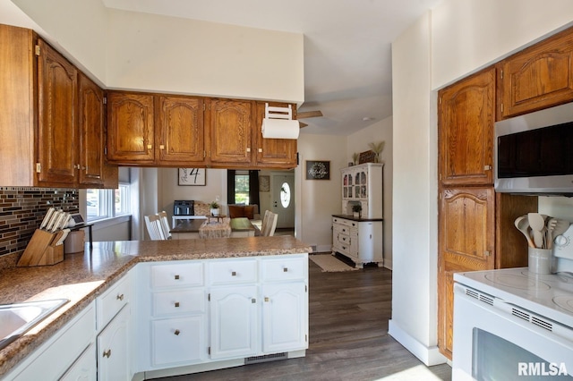 kitchen featuring stainless steel microwave, a peninsula, white electric range oven, wood finished floors, and decorative backsplash