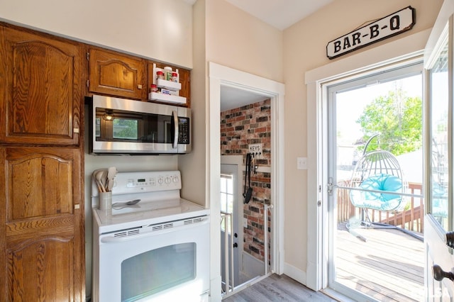 kitchen with stainless steel microwave, white range with electric stovetop, brown cabinetry, light countertops, and light wood-style floors