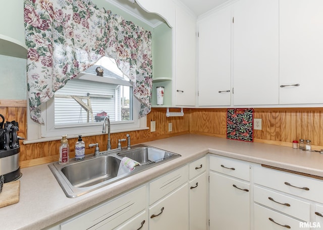 kitchen with a sink, crown molding, white cabinetry, and light countertops
