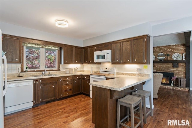 kitchen featuring white appliances, a sink, a peninsula, dark brown cabinetry, and dark wood-style floors