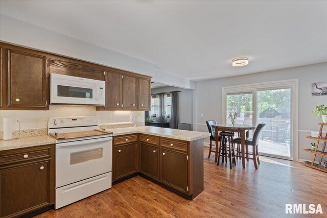 kitchen featuring white appliances, a peninsula, wood finished floors, and dark brown cabinetry