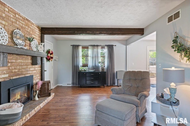 living area with wood finished floors, beamed ceiling, a textured ceiling, a brick fireplace, and baseboards