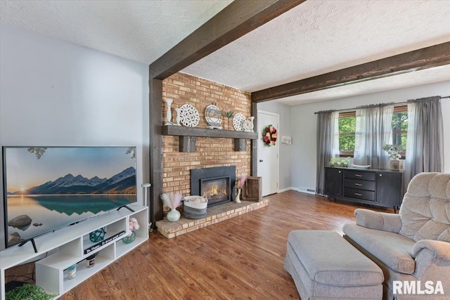 living room with a textured ceiling, beam ceiling, wood finished floors, and a brick fireplace