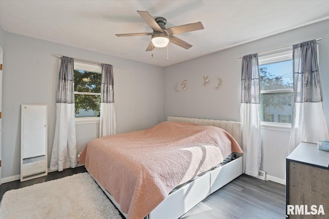 bedroom with multiple windows, wood finished floors, and baseboards
