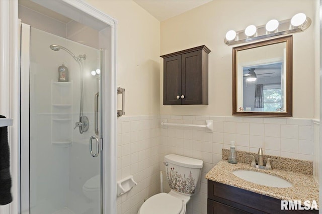 full bathroom featuring toilet, a shower stall, a wainscoted wall, tile walls, and vanity