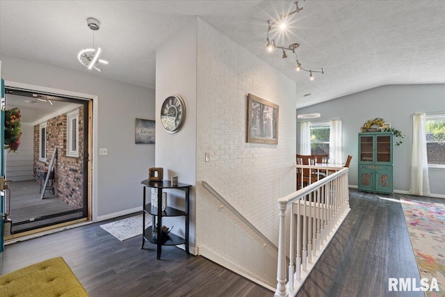 entryway featuring wood finished floors, lofted ceiling, baseboards, and a textured ceiling