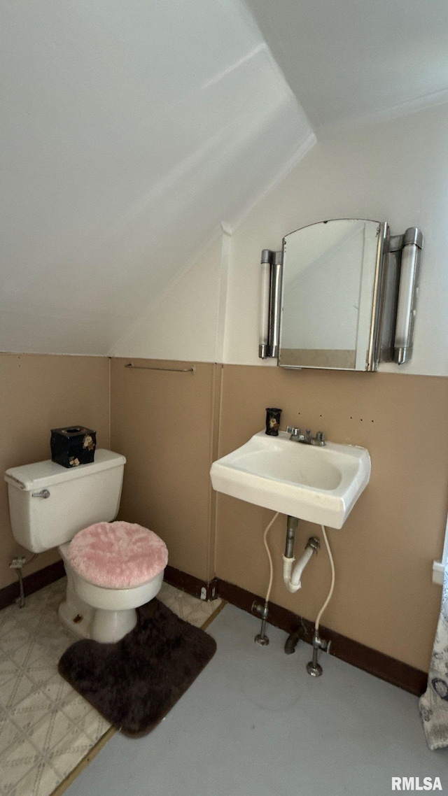 bathroom featuring vaulted ceiling, baseboards, toilet, and a sink