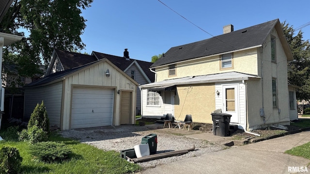 back of property with an outdoor structure, driveway, stucco siding, and a chimney