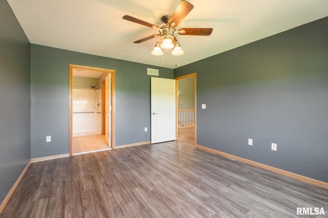 unfurnished bedroom featuring wood finished floors, baseboards, ensuite bathroom, and a ceiling fan